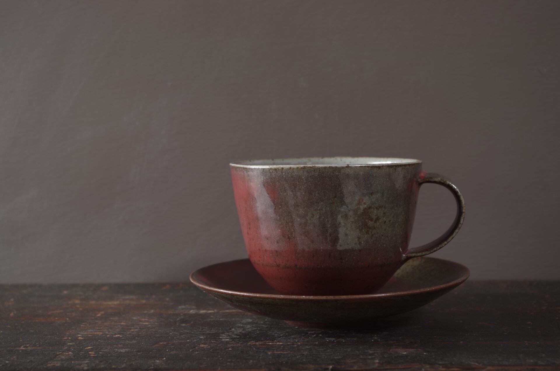 thrown dark stoneware cup and saucer with reduction fired copper red glaze by James and Tilla Waters in Wales, UK