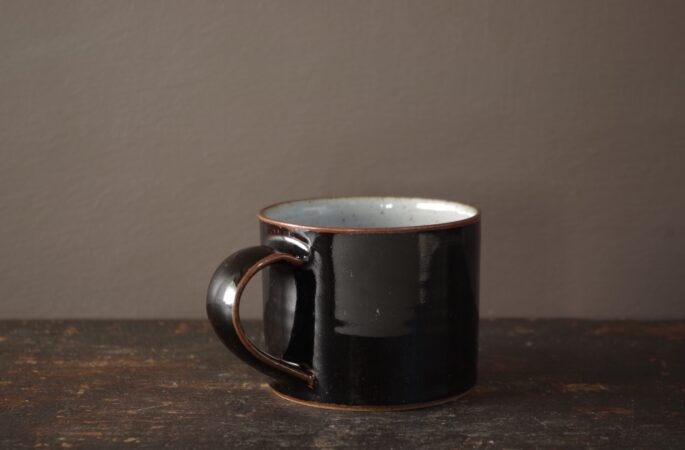 Thrown stoneware coffee cup with pulled handle and black tenmoku glaze by James and Tilla Waters in Wales, UK