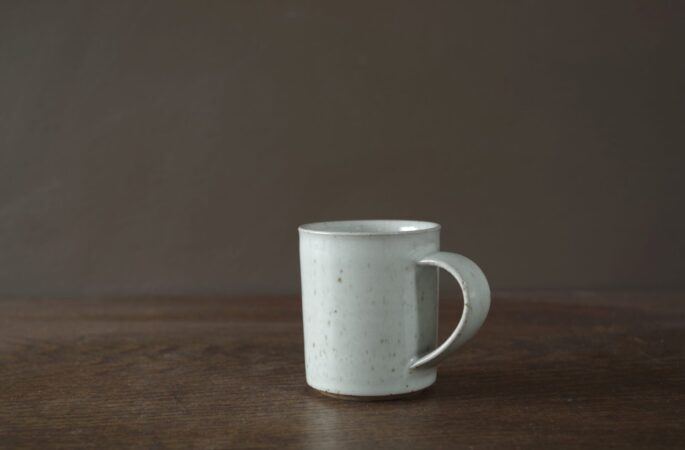 wheel thrown reduction fired stoneware coffee cup with off-white glaze and pulled handle by award winning potters James and Tilla Waters in Carmartheshire, Wales, UK