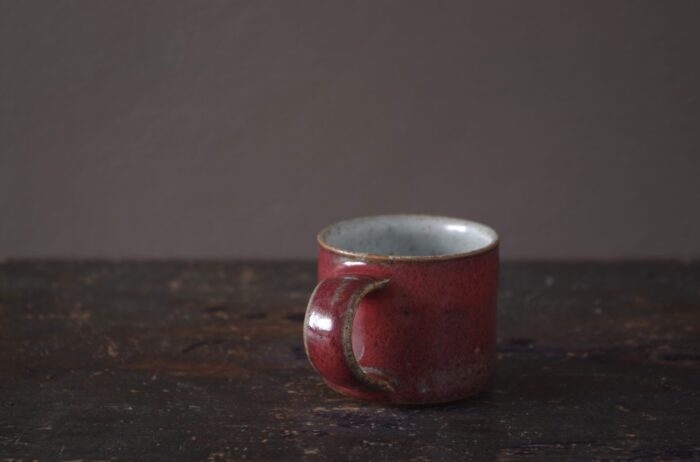 reduction fired wheel thrown stoneware espresso cup with pulled handle and copper red glaze by award winning potters James and Tilla Waters in their studio in Carmarthenshire, Wales