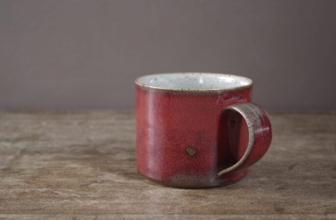 reduction fired, wheel thrown stoneware breakfast mug with pulled handle and copper red glaze with an iron spot by award winning potters James and Tilla Waters in their studio in Carmarthenshire Wales