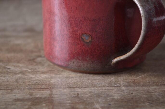 reduction fired, wheel thrown stoneware breakfast mug with pulled handle and copper red glaze with an iron spot by award winning potters James and Tilla Waters in their studio in Carmarthenshire Wales