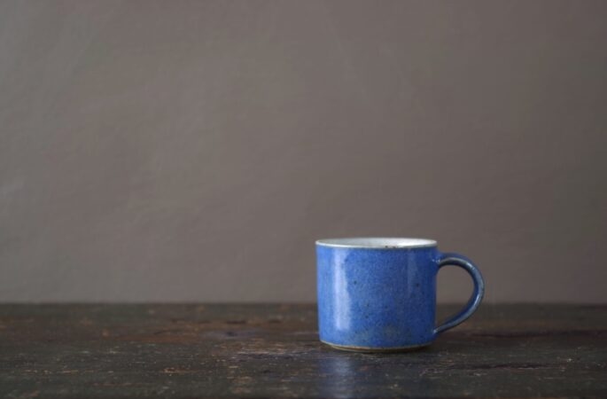 reduction fired wheel thrown stoneware espresso cup with pulled handle and mid blue glaze by award winning potters James and Tilla Waters in their studio in Carmarthenshire, Wales