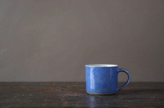 reduction fired wheel thrown stoneware espresso cup with pulled handle and mid blue glaze by award winning potters James and Tilla Waters in their studio in Carmarthenshire, Wales