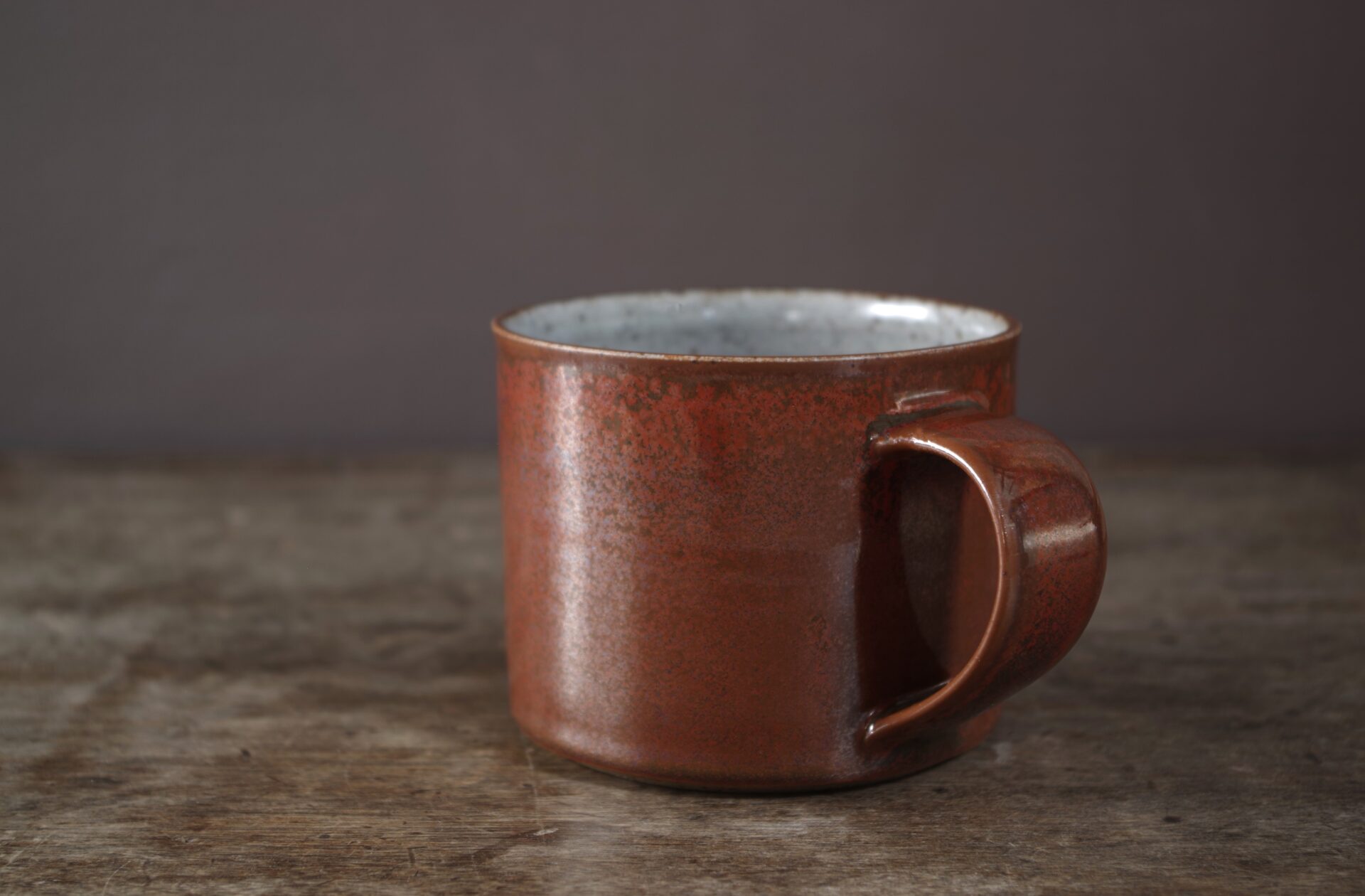reduction fired, wheel thrown stoneware breakfast mug with pulled handle and rust coloured persimmon glaze by award winning potters James and Tilla Waters in their studio in Carmarthenshire Wales