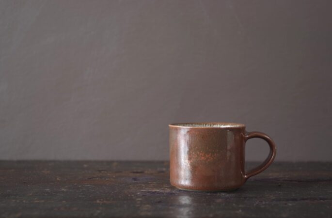 reduction fired wheel thrown stoneware espresso cup with pulled handle and persimmon glaze by award winning potters James and Tilla Waters in their studio in Carmarthenshire, Wales