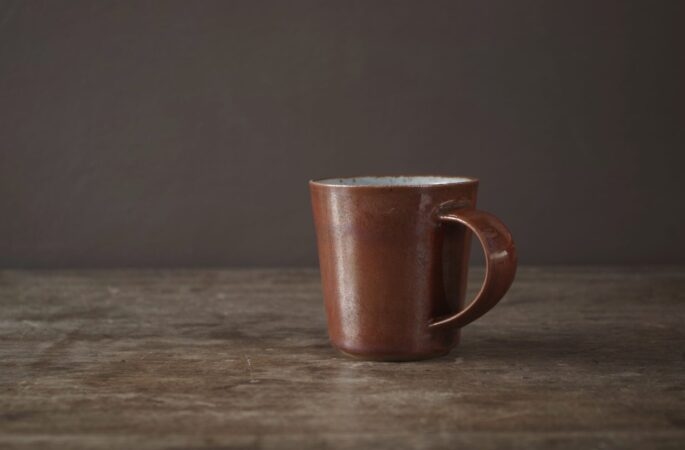 reduction fired stoneware flared coffee cup with rust coloured persimmon glaze and pulled handle by award winning potters James and Tilla Waters in Carmartheshire, Wales, UK