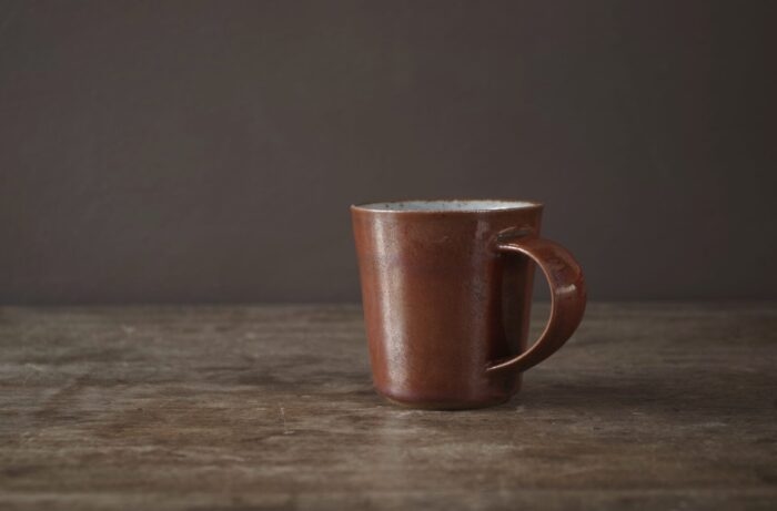 reduction fired stoneware flared coffee cup with rust coloured persimmon glaze and pulled handle by award winning potters James and Tilla Waters in Carmartheshire, Wales, UK