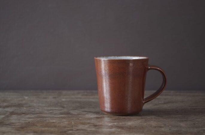 reduction fired stoneware flared coffee cup with rust coloured persimmon glaze and pulled handle by award winning potters James and Tilla Waters in Carmartheshire, Wales, UK