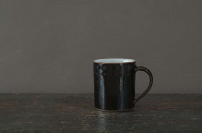 wheel thrown reduction fired stoneware coffee cup with black tenmoku glaze and pulled handle by award winning potters James and Tilla Waters in Carmartheshire, Wales, UK