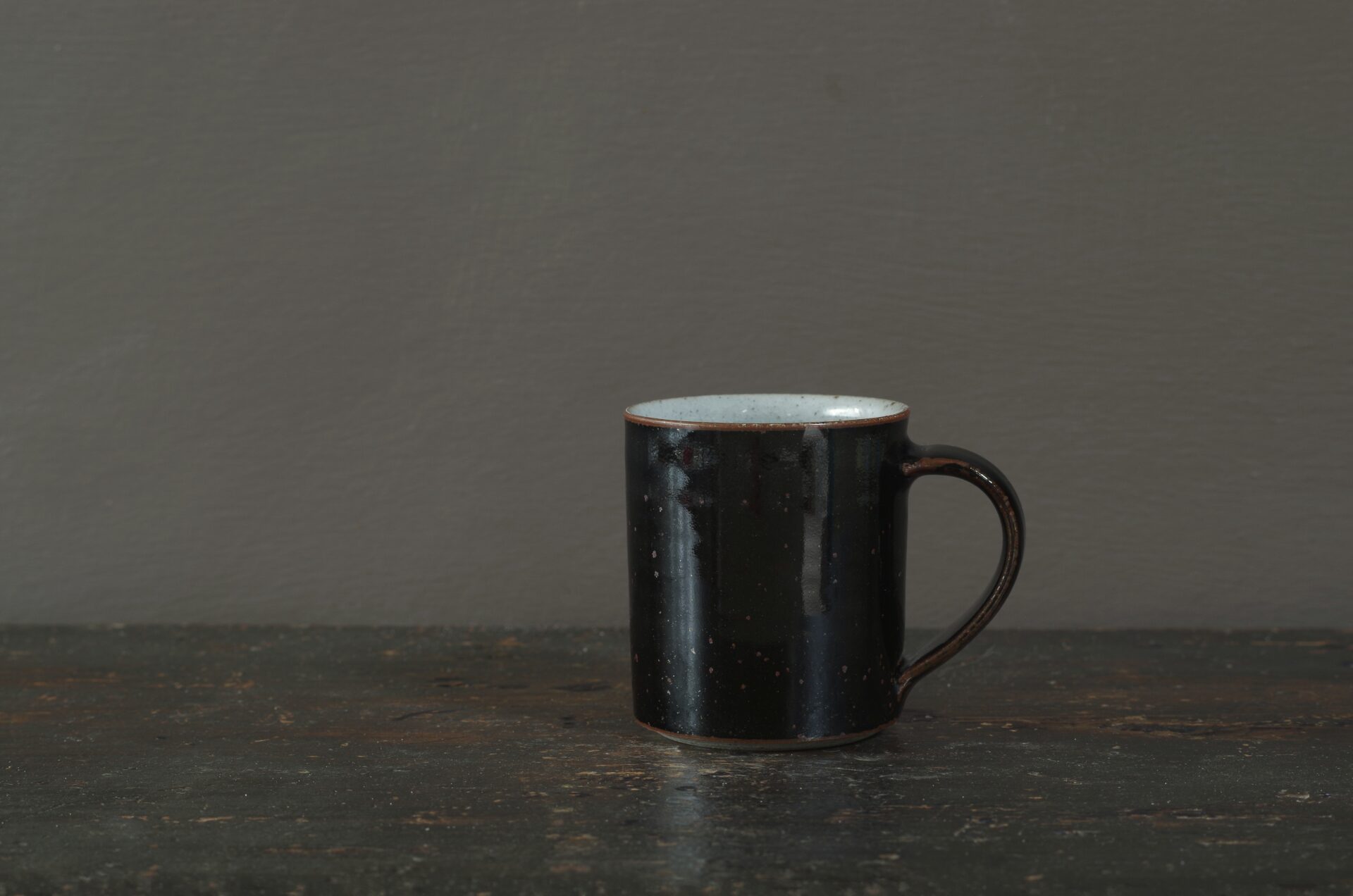 wheel thrown reduction fired stoneware coffee cup with black tenmoku glaze and pulled handle by award winning potters James and Tilla Waters in Carmartheshire, Wales, UK