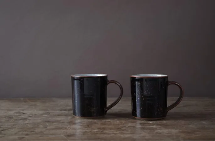 wheel thrown reduction fired stoneware coffee cup with black tenmoku glaze and pulled handle by award winning potters James and Tilla Waters in Carmartheshire, Wales, UK