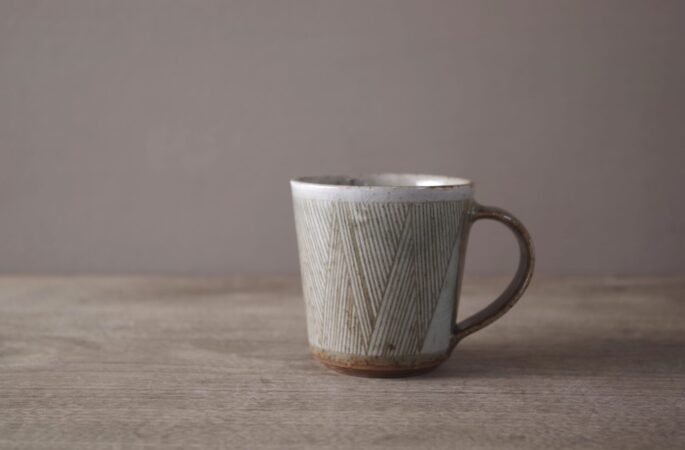 wheel thrown reduction fired stoneware coffee cup with sgraffito geometric decoration and pulled handle by award winning potters James and Tilla Waters in Carmartheshire, Wales, UK