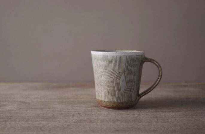 wheel thrown reduction fired stoneware coffee cup with sgraffito geometric decoration and pulled handle by award winning potters James and Tilla Waters in Carmartheshire, Wales, UK