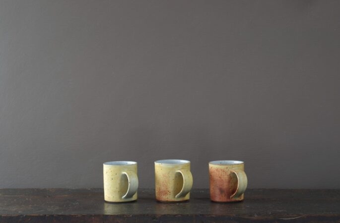 wheel thrown reduction fired stoneware coffee cup with rusty yellow coloured glaze and pulled handle by award winning potters James and Tilla Waters in Carmartheshire, Wales, UK