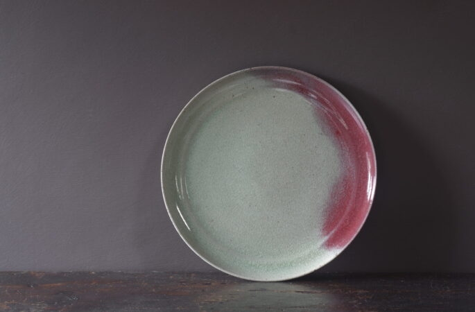 large thrown stoneware dinner plate with patchy copper red glaze, fired in reduction by award winning studio potters James and Tilla Waters in Carmarthenshire, Wales UK