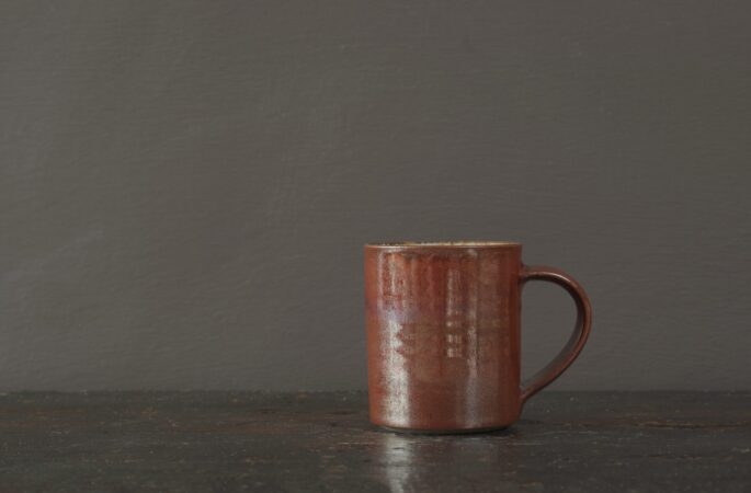 wheel thrown reduction fired stoneware coffee cup with rust coloured persimmon glaze and pulled handle by award winning potters James and Tilla Waters in Carmartheshire, Wales, UK
